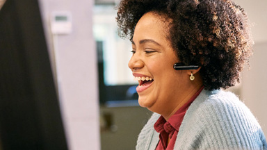 Woman wearing a headset sitting at computer desk laughing 