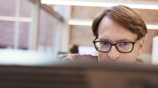 Man with glasses peering over computer