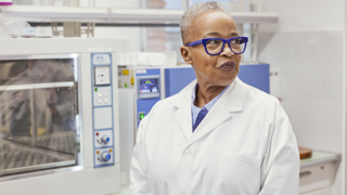 female scientist in lab with machines behind her 