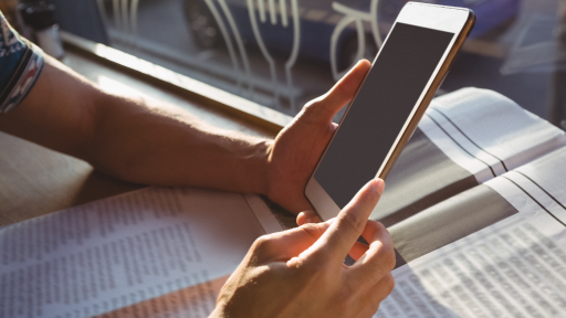 Arms holding tablet with newspaper in background