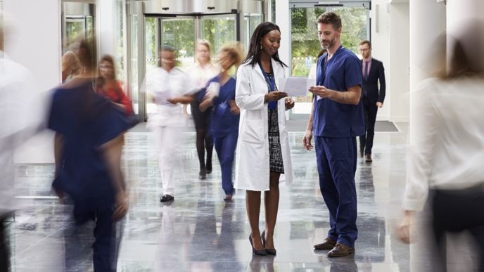 Doctor and nurse chatting in hall surrounded by blurred people