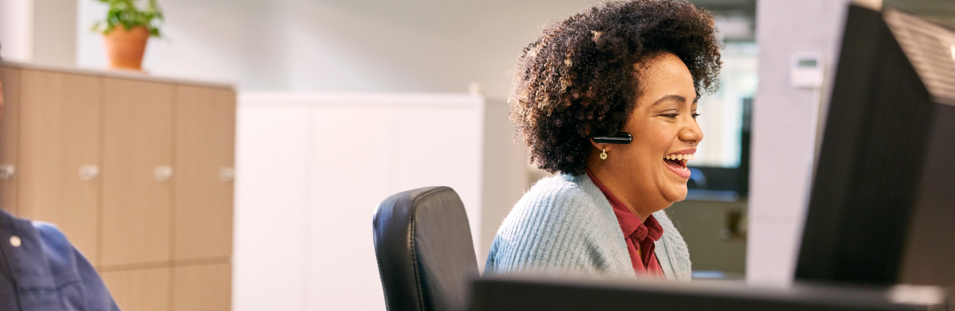 Woman wearing a headset sitting at computer desk laughing 