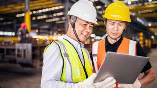 Two male coworkers in hard hats looking at document 