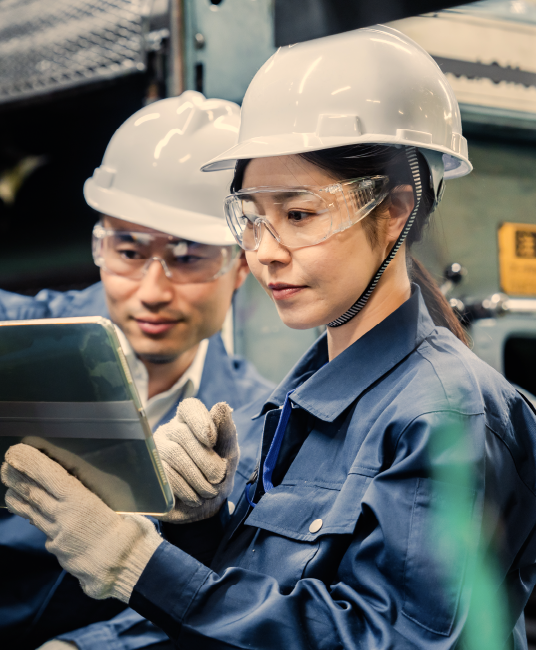 A man and female working together in a manufacturing building with hardhats