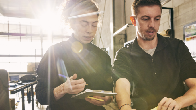 A female and male coworkers chatting over a clipboard 