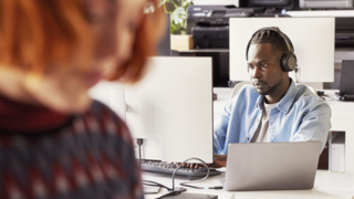 Women blurred in foreground and man sitting behind computer at office desk