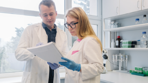 Two people wearing white lab coats reviewing documents